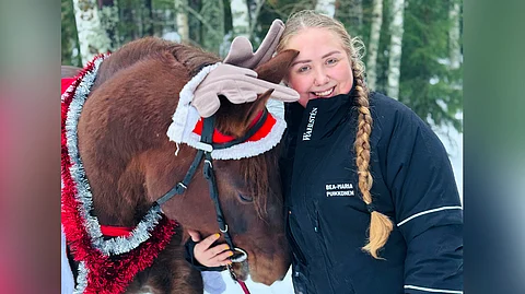 Bea-Maria Puikkonen poseeraa yhdessä oman hevosensa Väyrylän Hermannin kanssa jouluisessa kuvassa.