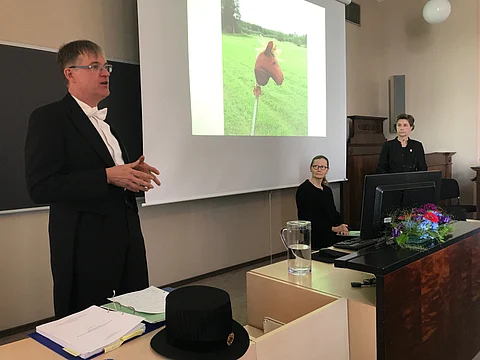 Väitöskirjan esittelyosuus tehty ja itse väitös alkamassa. Vastaväittäjä, dosentti Petteri Nieminen, kustos tohtori Outi Vainio ja väittelijä Raija Hallamaa Helsingin yliopiston salissa XII. Vaikka sairaus on iänikuisen vanha, tutkimusaihe on uusi ja haastaa totuttuja käsityksiä. Vastapainona kuvassa Hallamaan vanha keppihevonen, jolla on ikää jo yli 50 vuotta.